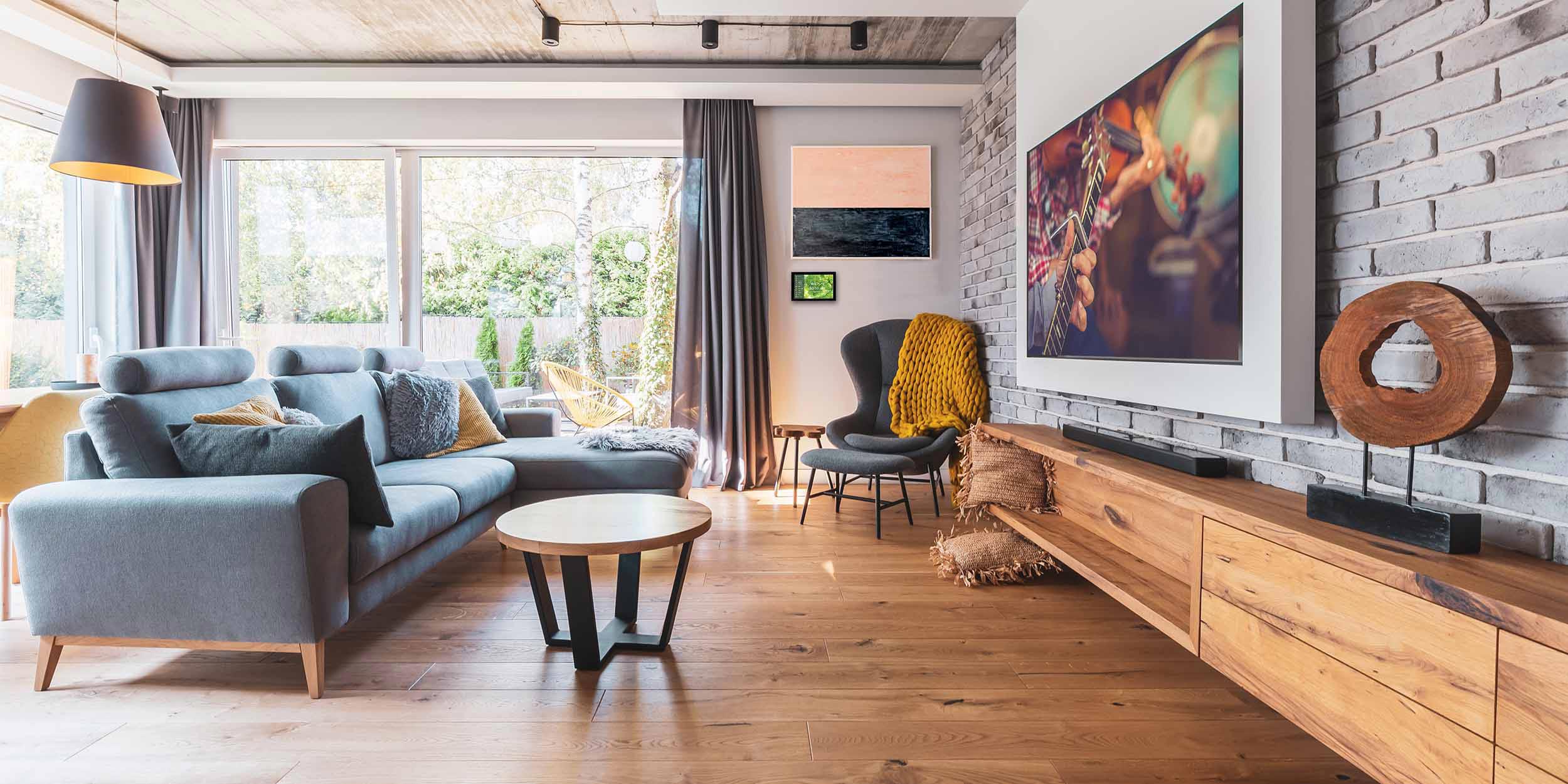 A cozy, modern living room with gray sofas, wooden floor, and a TV mounted on a brick wall.